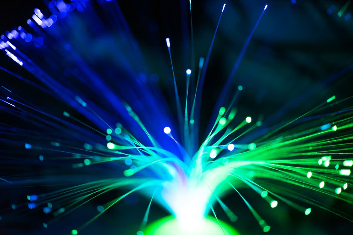 Macro photograph of illuminated fiber-optic strands fanning out, lit green and blue.