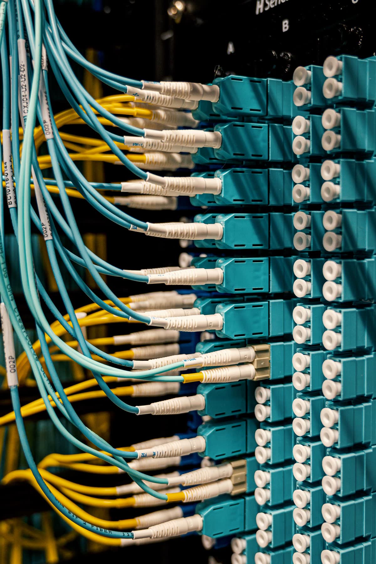 Fiber-optic patch panel in a network rack, dense with teal LC connectors and cabling.